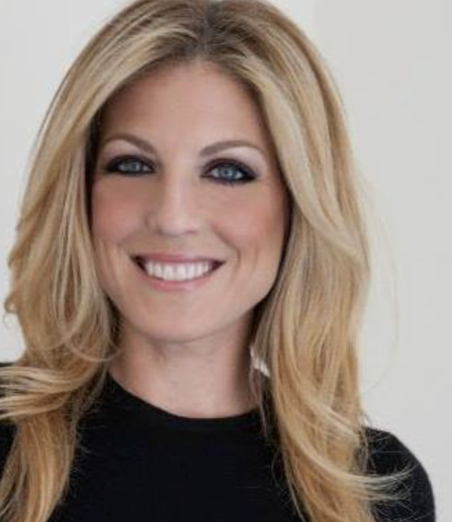 Headshot of a woman in front of a white background. She has dirty blonde long hair is smiling while looing directly at the camera. She is also wearing a black shirt with a crew neck.